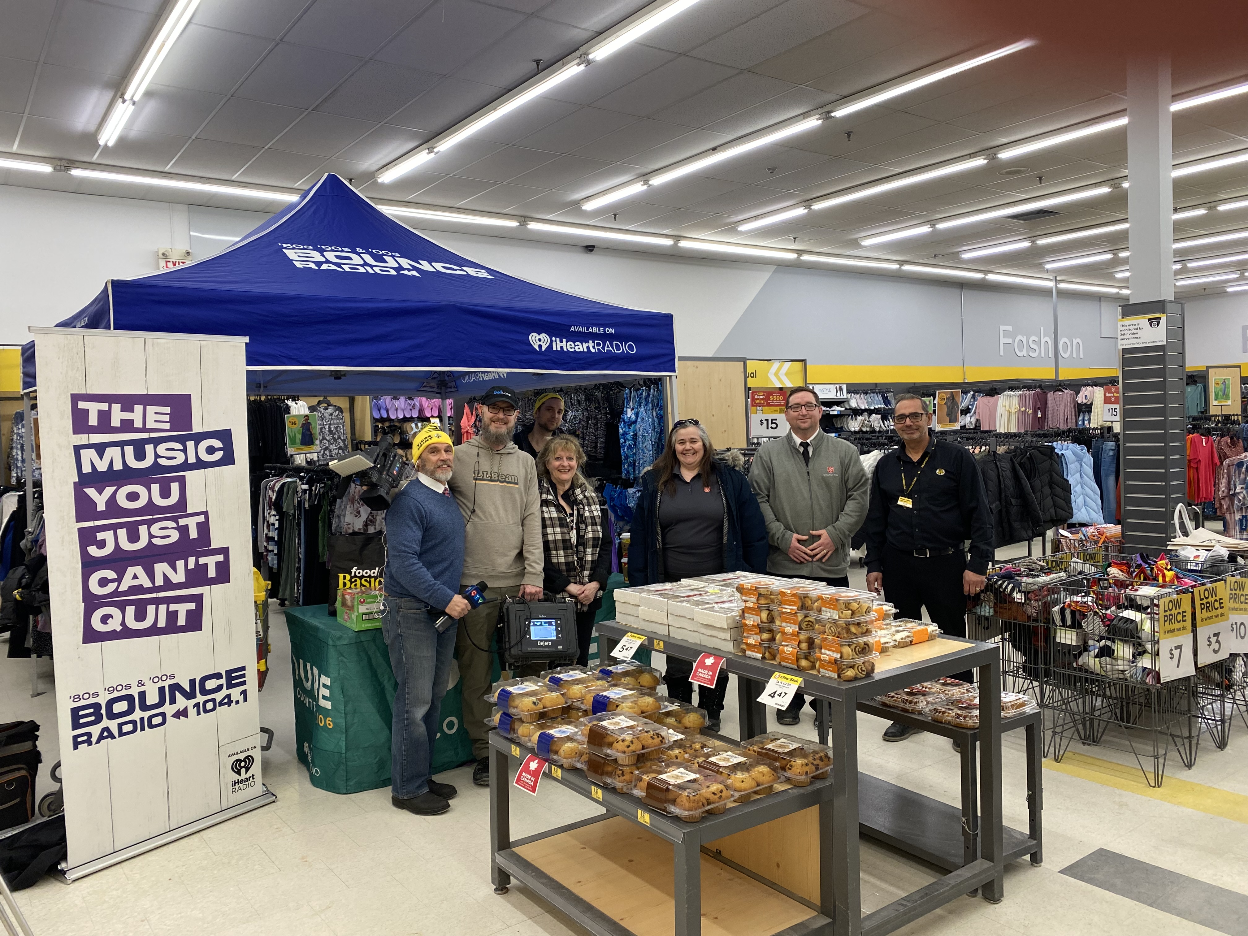 Group of people standing beside a promotional booth and table of packaged baked goods inside a retail store.