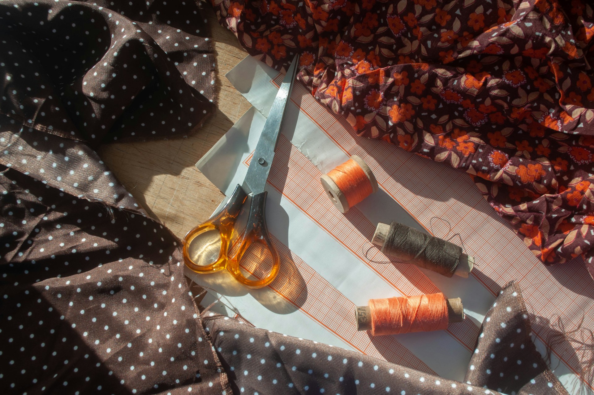 Scissors, thread spools, and patterned fabric laid out on a table for sewing.