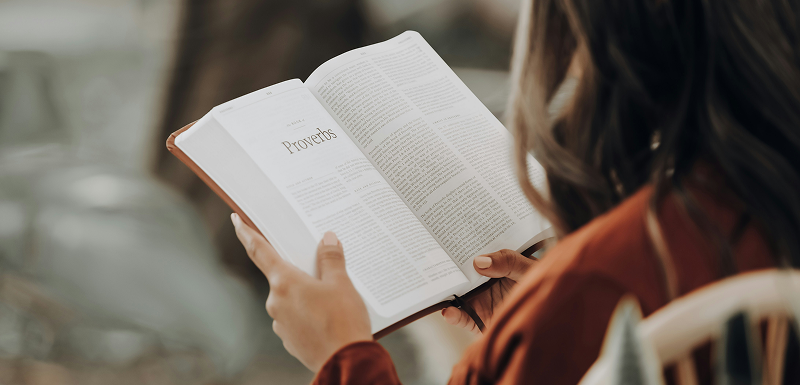 Close-up of a person holding and reading an open Bible turned to the book of Proverbs.