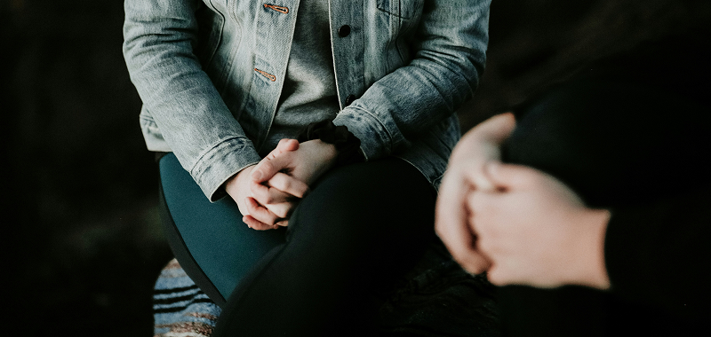 Close-up of two people seated facing each other with hands clasped, suggesting conversation or support.